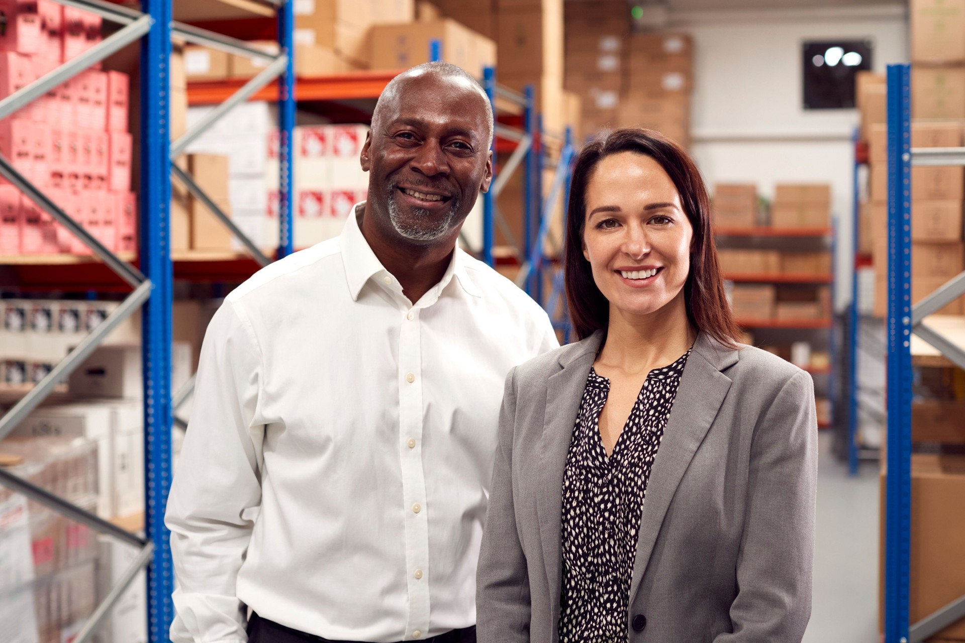 Portrait Of Male And Female Team Leaders Standing By Shelves In Warehouse